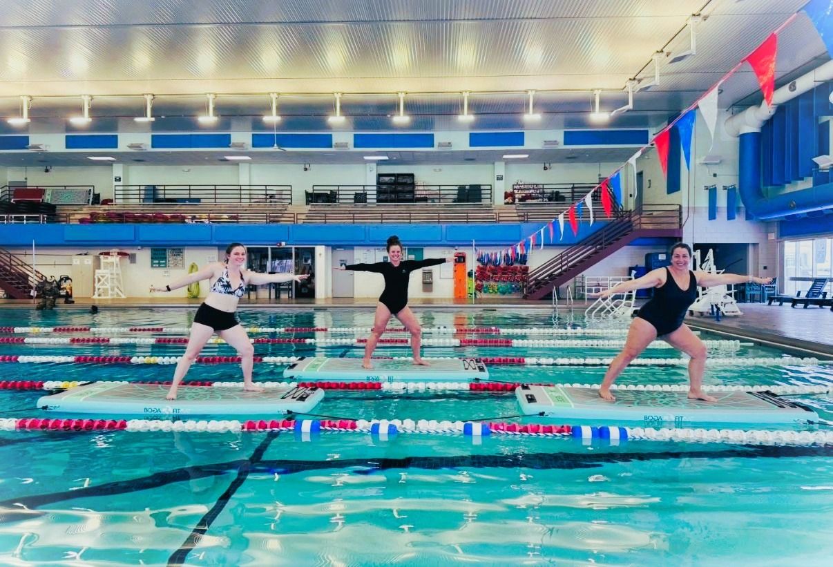 three women standing on paddle boards inside of a pool