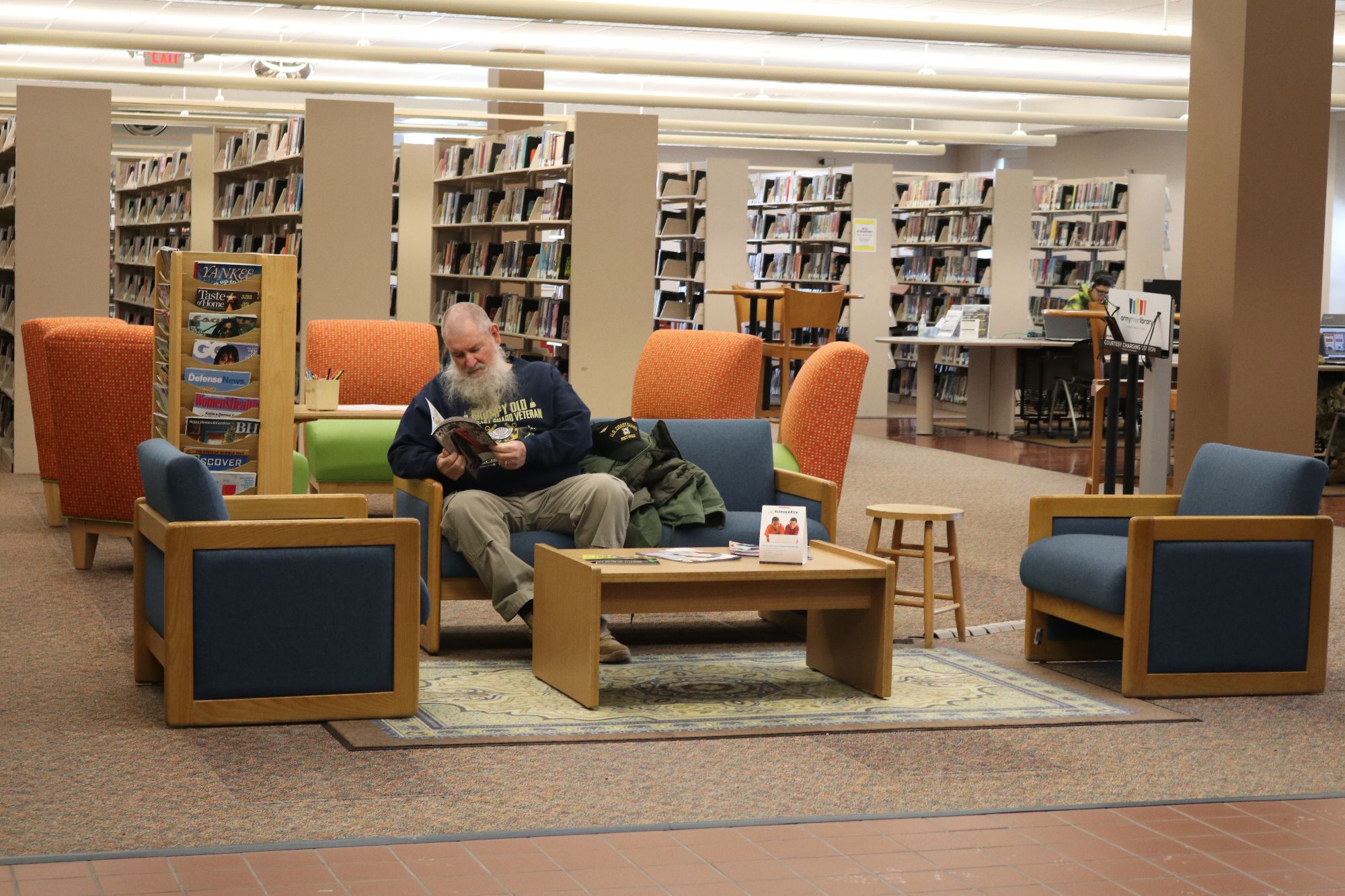 gentleman sitting in the reading area of the library surround by book shelves and other seats